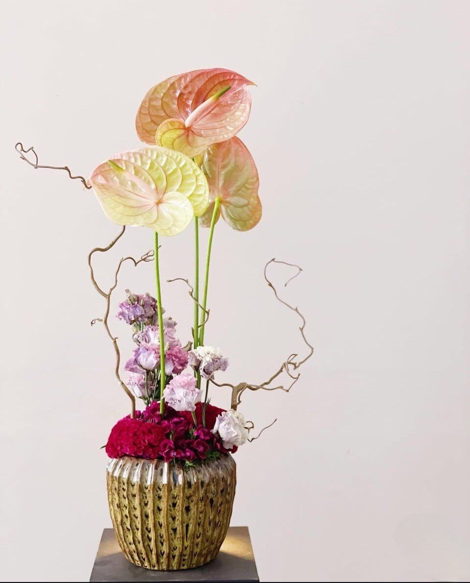 Composizione scultorea di anthurium pesca e rami intrecciati in un vaso dorato